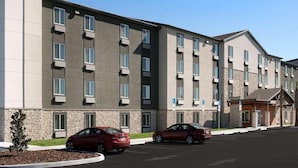 A multi-story hotel with a modern design, featuring a parking lot with two cars and a small landscaped area with a tree. - Woodspring Suites Riverside Norco (Norco)