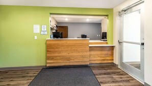 Un espace d’accueil avec un comptoir en bois, des murs verts et une porte en verre.