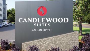 A sign for Candlewood Suites, an IHG hotel, with a red logo, surrounded by a landscaped garden with various colorful flowers.