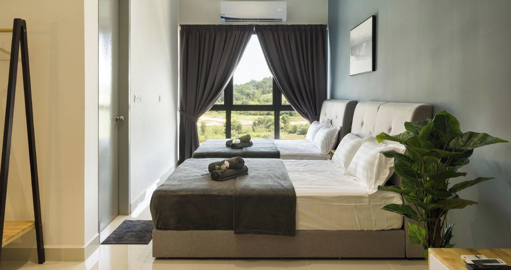 A hotel room with two beds, a large window with curtains, a plant, and a door.