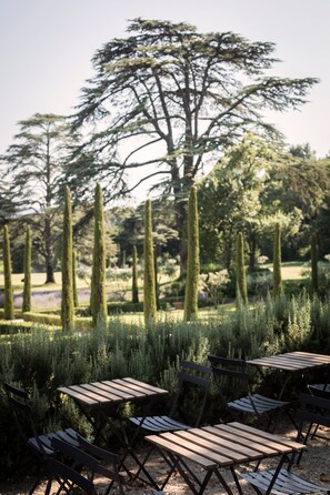 A garden with neatly arranged wooden tables and chairs, surrounded by trimmed hedges and tall trees. - Domaine de Fontenille (Lauris)