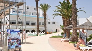 Un resort con zona de piscina, sillas de descanso, palmeras y un letrero que dice 'Quind Adventures Boot Trip'.