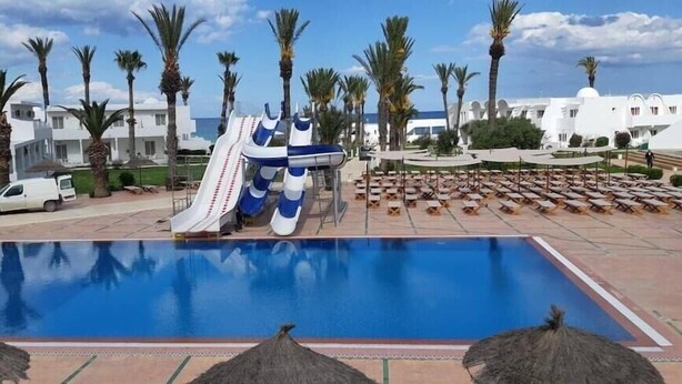 Piscina con tobogán de agua, palmeras y sillas de descanso.