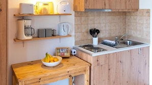 Cocina compacta con armarios de madera, horno empotrado, microondas, cafetera y lavabo.