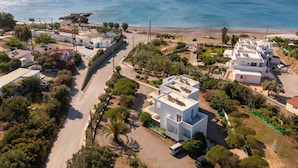 Vista aérea de una zona residencial costera con casas blancas, un camino estrecho y una playa al fondo.