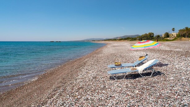 Una playa de guijarros con dos sillones a rayas y una sombrilla colorida.