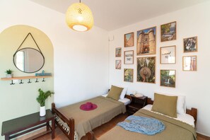 A cozy bedroom with two beds, a hanging light fixture, a mirror, and a wall adorned with travel-themed pictures. - Tselios Apartments & Studios (Rhodes)