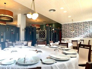A restaurant with round tables set for dining, a patterned wall, and a ceiling with recessed lighting. - Don Polvoron (Estepa)