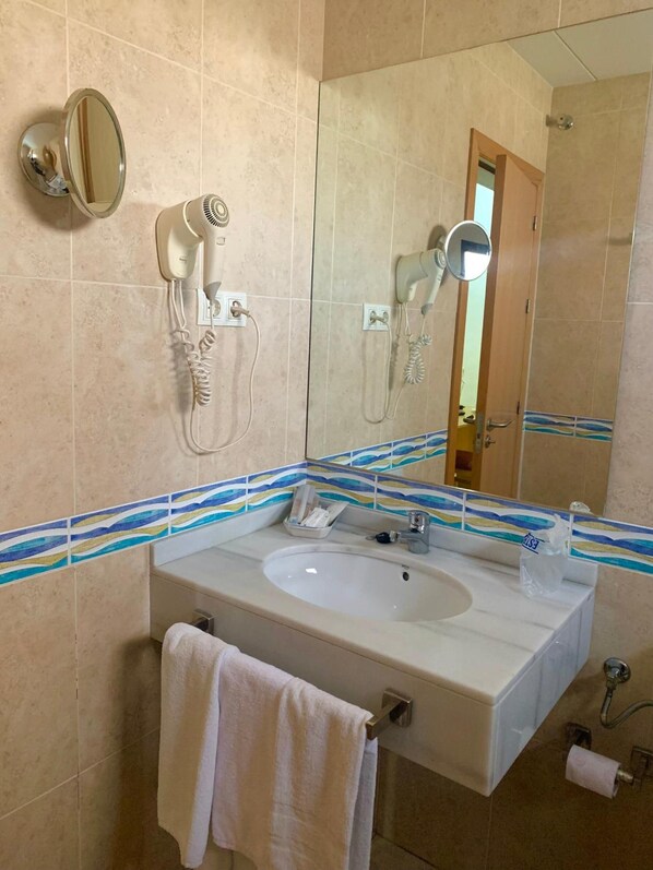 A bathroom with a sink, mirror, hair dryer, and shower. - Don Polvoron (Estepa)