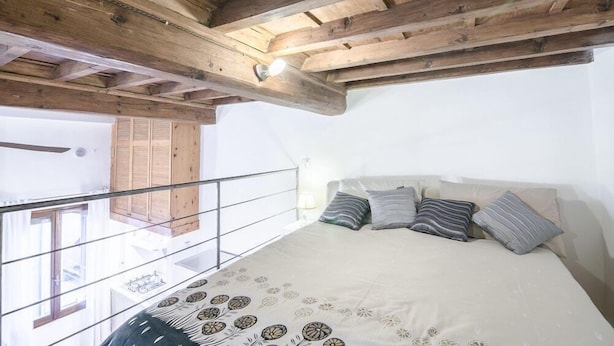 A bedroom with a wooden ceiling, a bed with patterned bedding, and a balcony with a railing. - San Niccolo Loft (Florence)