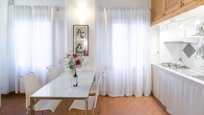 A dining area with a white table and chairs, a vase with flowers, and a kitchen with white cabinets and a stove. - San Niccolo Loft (Florence)