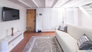 A modern living room with a flat-screen TV mounted on the wall, a white sofa with patterned cushions, a wooden door, and a white wardrobe. - San Niccolo Loft (Florence)