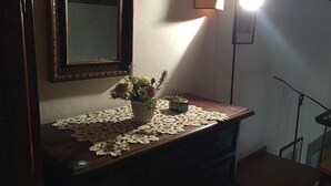 Une commode en bois, sur laquelle repose un chemin de table en dentelle, un vase avec des fleurs et un miroir.