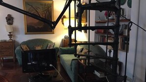 Un salon chaleureux avec une lampe de style vintage, un fauteuil vert, une table d’appoint en bois et une bibliothèque remplie de livres et d’objets décoratifs.