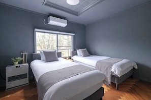 A modern hotel room with two beds, a large window, a heater, and a small table with a plant.