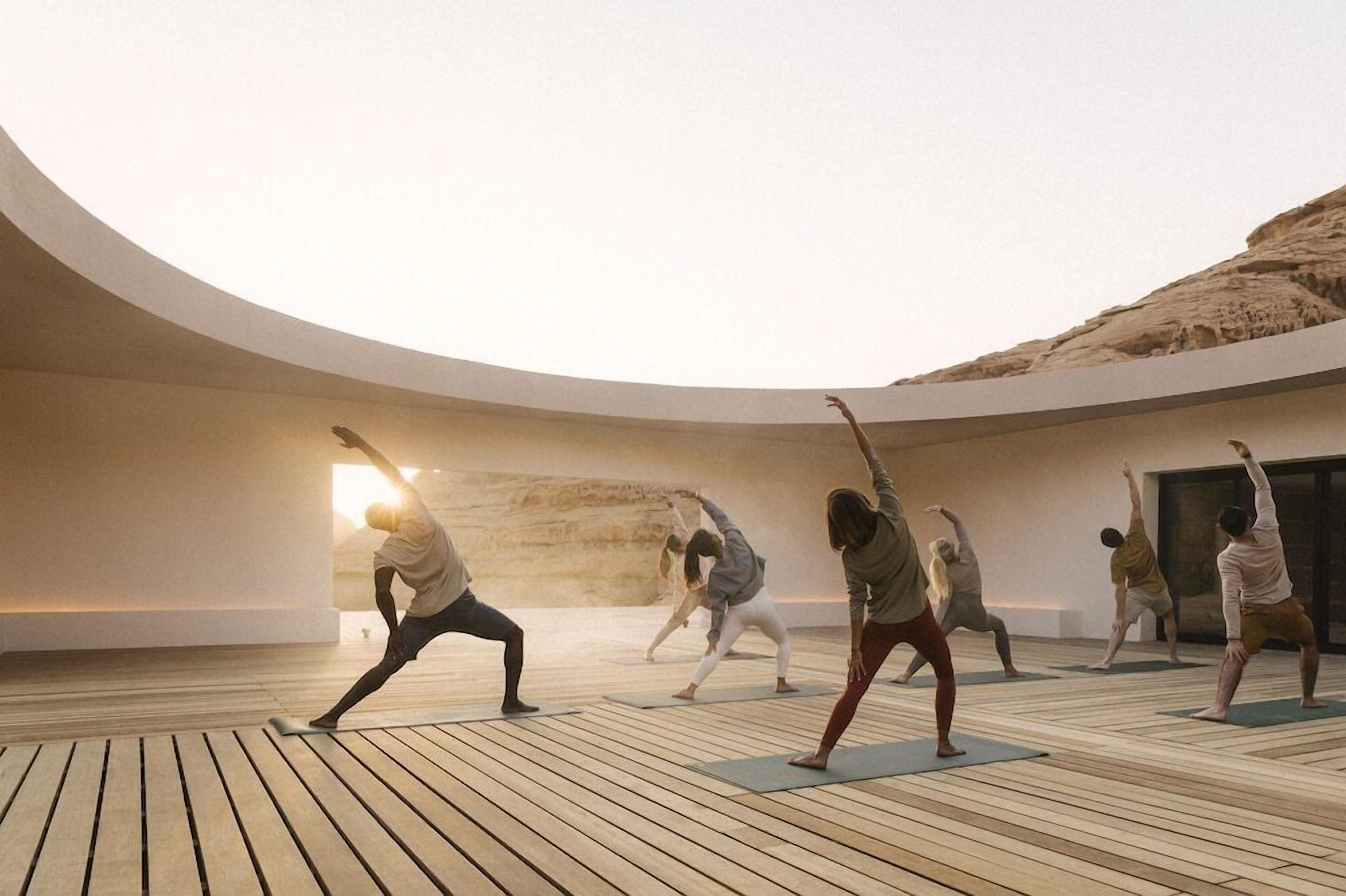 Un grupo de personas practicando yoga en una sala amplia y moderna, con piso de madera y una pared grande y curva.