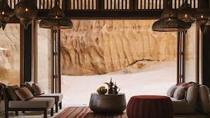 A cozy room with a large window, a sofa, a red ottoman, and a decorative bowl on a rug.