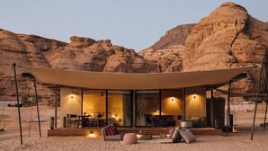 A desert resort with a covered outdoor seating area, a dining space, and a large rock formation in the background.