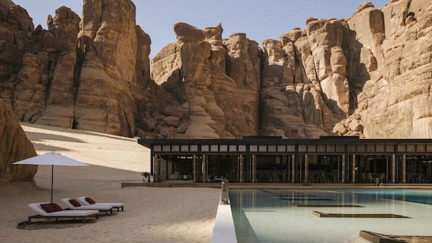 A pool area with lounge chairs and a building with large windows.