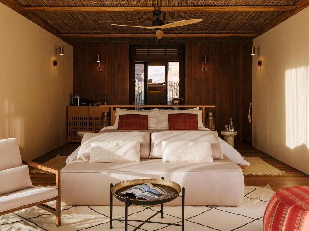 A bedroom with a large bed, a wooden ceiling, and a view through a window.
