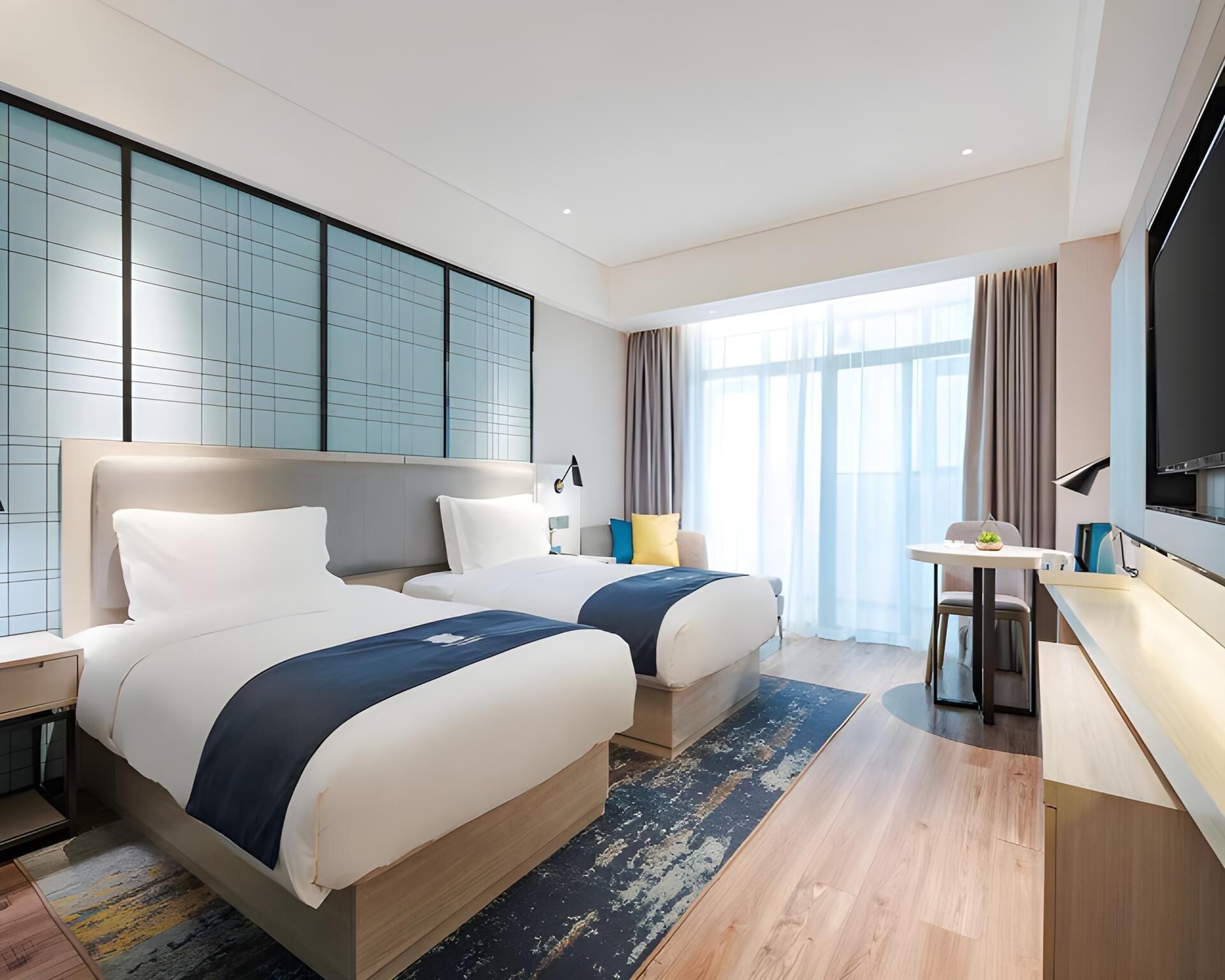 A modern hotel room with two beds, a desk, a TV, and large windows.