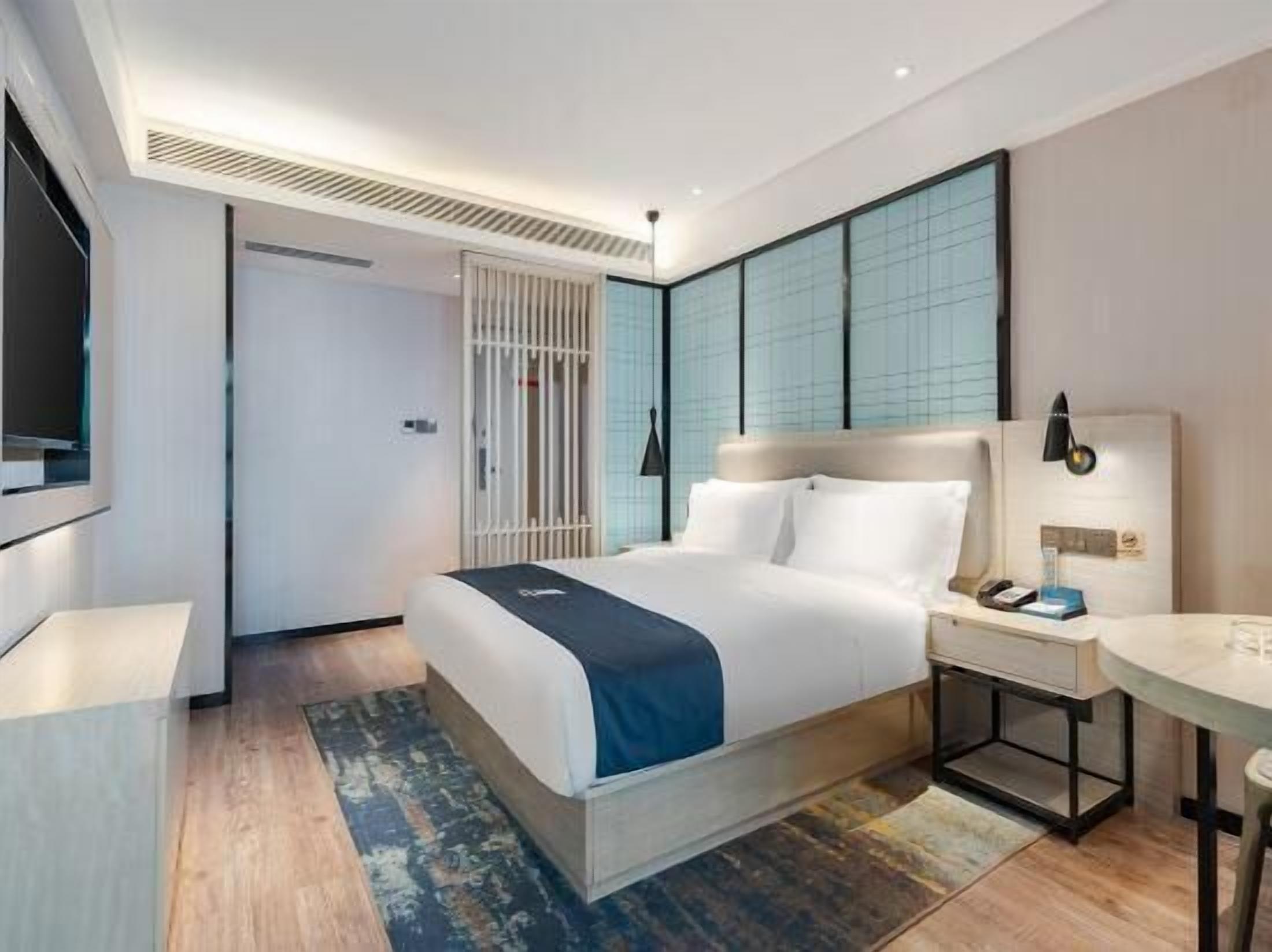 A modern hotel room with a large bed, bedside table, and a TV.