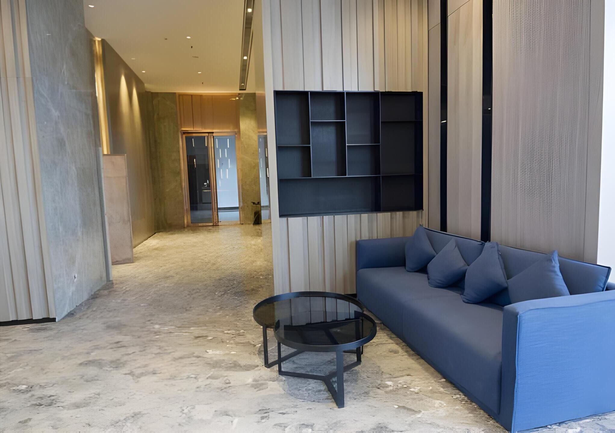 A modern living room with a blue sofa, a glass coffee table, and a wall-mounted shelving unit.
