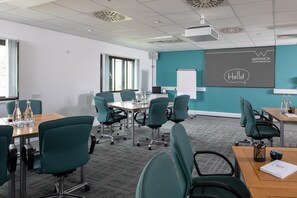A conference room with teal chairs, a wooden table, a projector, and a screen displaying "Warwick Conferences" and "Hello!". - Warwick Conferences - Radcliffe House (Coventry)