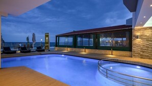 A modern indoor swimming pool with lounge chairs and a glass-enclosed area with a view of the sea. - Mare Hotel (Apokoronas)