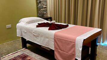 A massage room with a bed, a stone wall, a clock, and a curtain.
