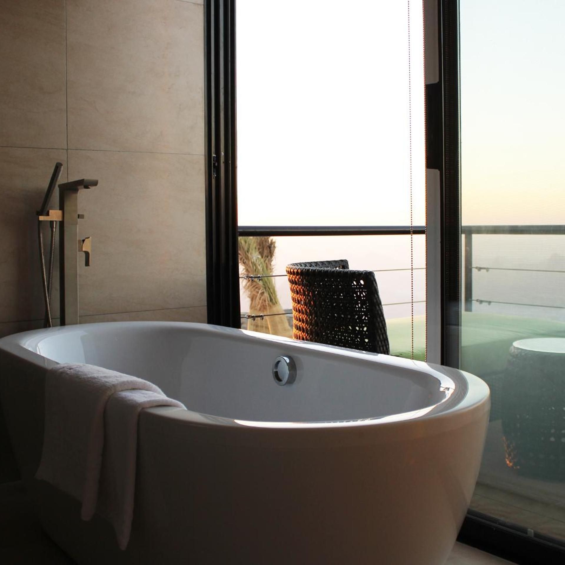 A modern bathroom with a freestanding bathtub, a towel, and a view of a balcony with outdoor furniture.