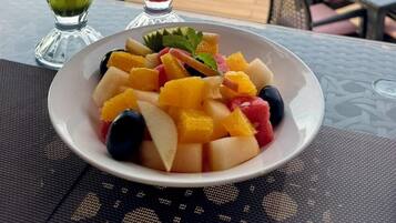 A table with two drinks, a plate of fruit, and a scenic view.