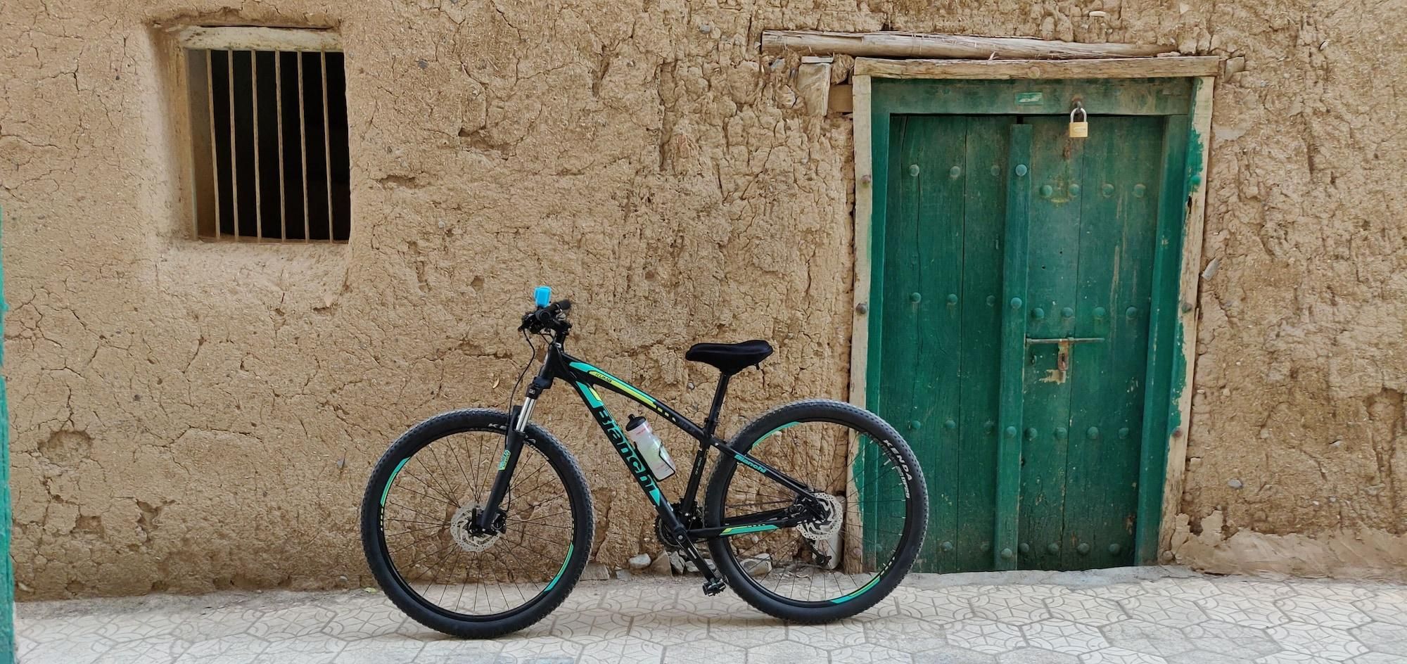 Uma bicicleta estacionada em frente a um edifício rústico com porta verde e janela com grades.