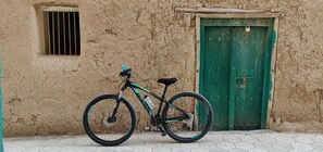 A bicycle parked in front of a rustic building with a green door and a barred window. - The View (Al Hamra)