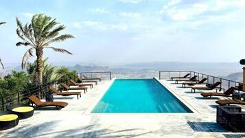 Uma piscina infinita no terraço com espreguiçadeiras e uma palmeira, com vista para uma paisagem montanhosa.