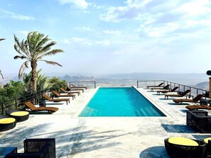 A rooftop infinity pool with lounge chairs and a palm tree, overlooking a mountainous landscape. - The View (Al Hamra)