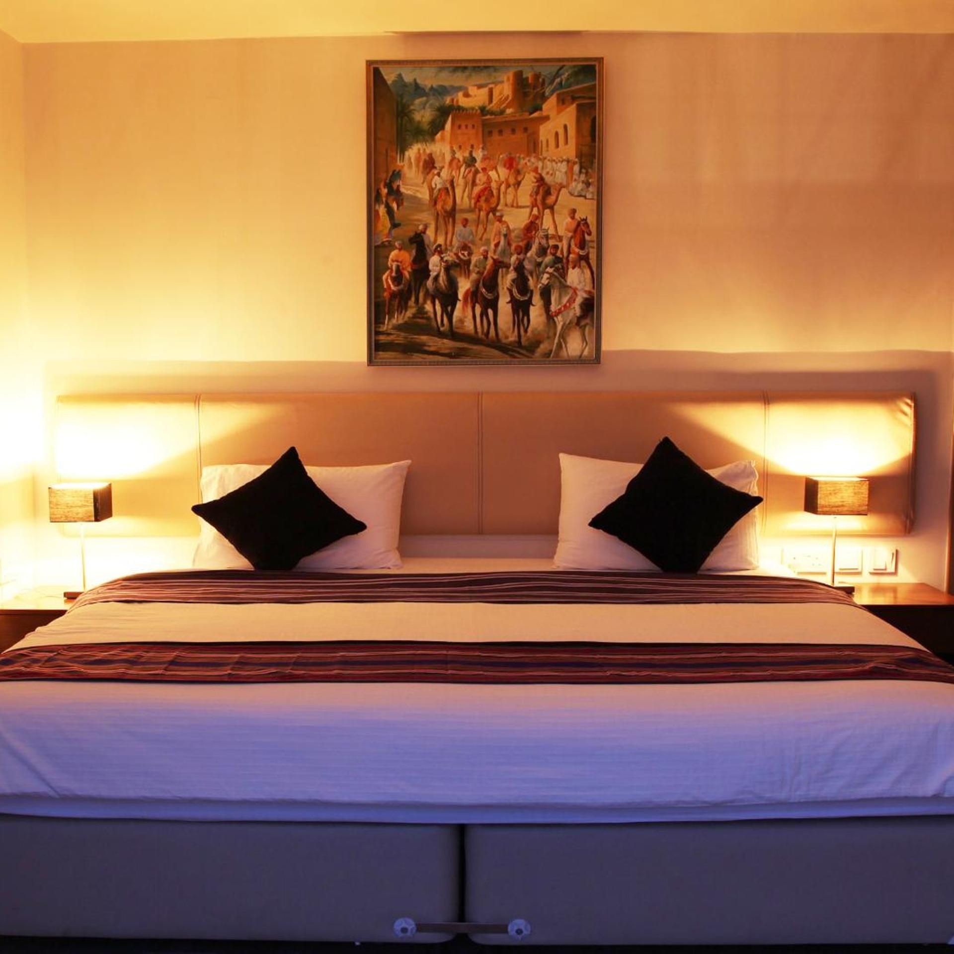 Habitación de hotel con una cama grande, dos almohadas negras, un cuadro en la pared y lámparas de noche.