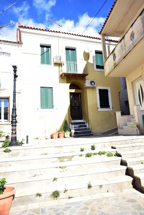 Um edifício com escadaria que leva a uma porta, uma varanda e uma janela com persianas verdes.