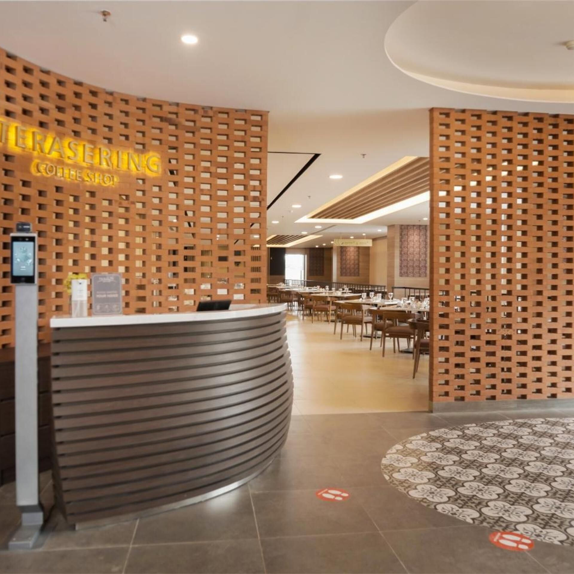 A reception desk with a modern design, a patterned floor, and a dining area with tables and chairs.