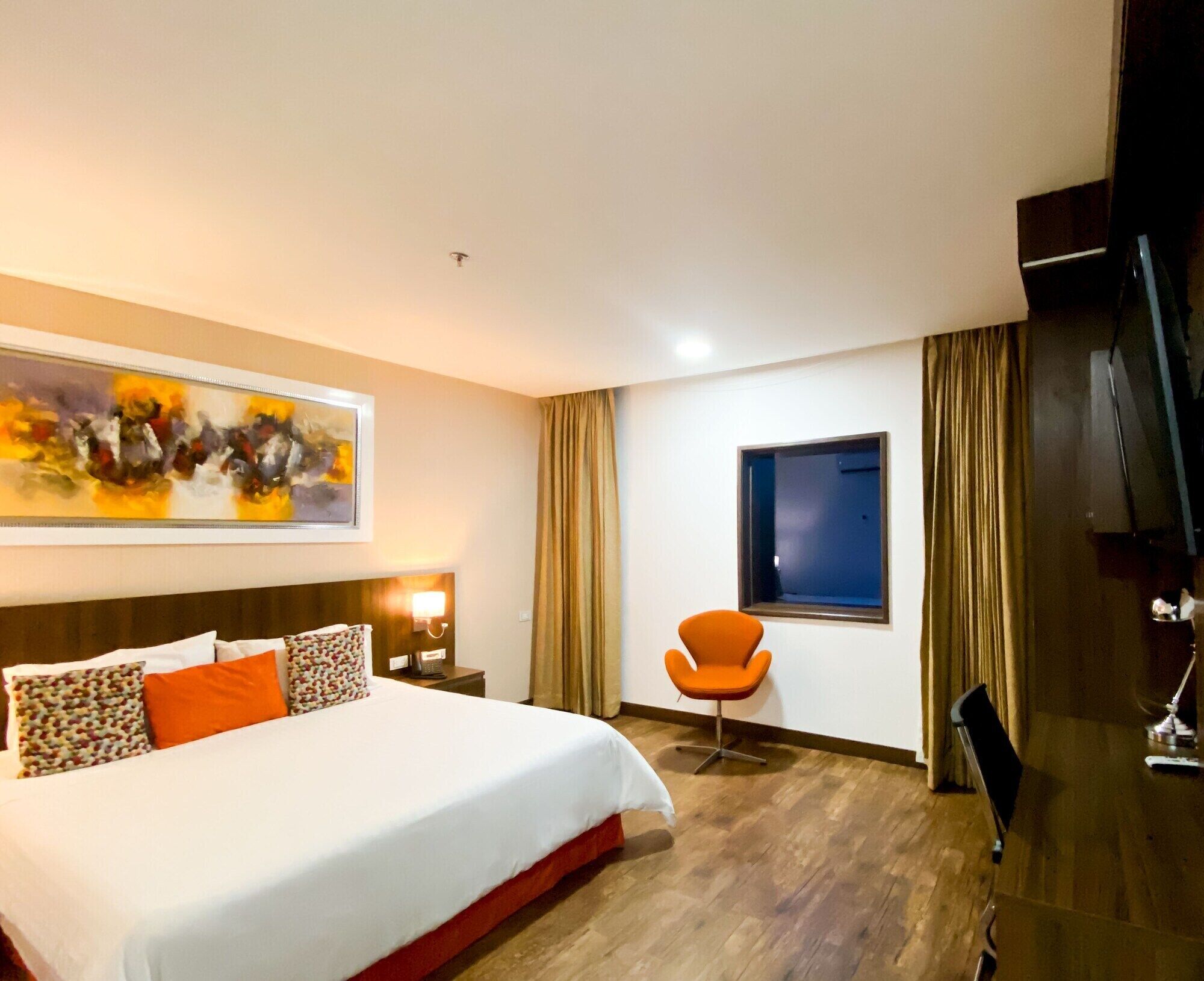 Een hotelkamer met een bed, een stoel, een televisie en een schilderij aan de muur.