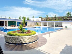 A modern hotel pool area with a circular mosaic planter, lounge chairs, and a landscaped wall. - Hotel Royal Elim Internacional (Palmira)
