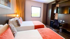 Ein Hotelzimmer mit zwei Betten, einem Schreibtisch, einem Stuhl, einem Fernseher und einem Fenster.