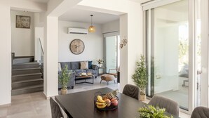 A modern living room with a dining area, a staircase, and a large glass door leading to an outdoor space.