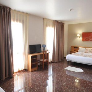 A hotel room with a bed, a desk with a chair, a television, and a wall-mounted lamp. - Maria Rosa (Pedrola)