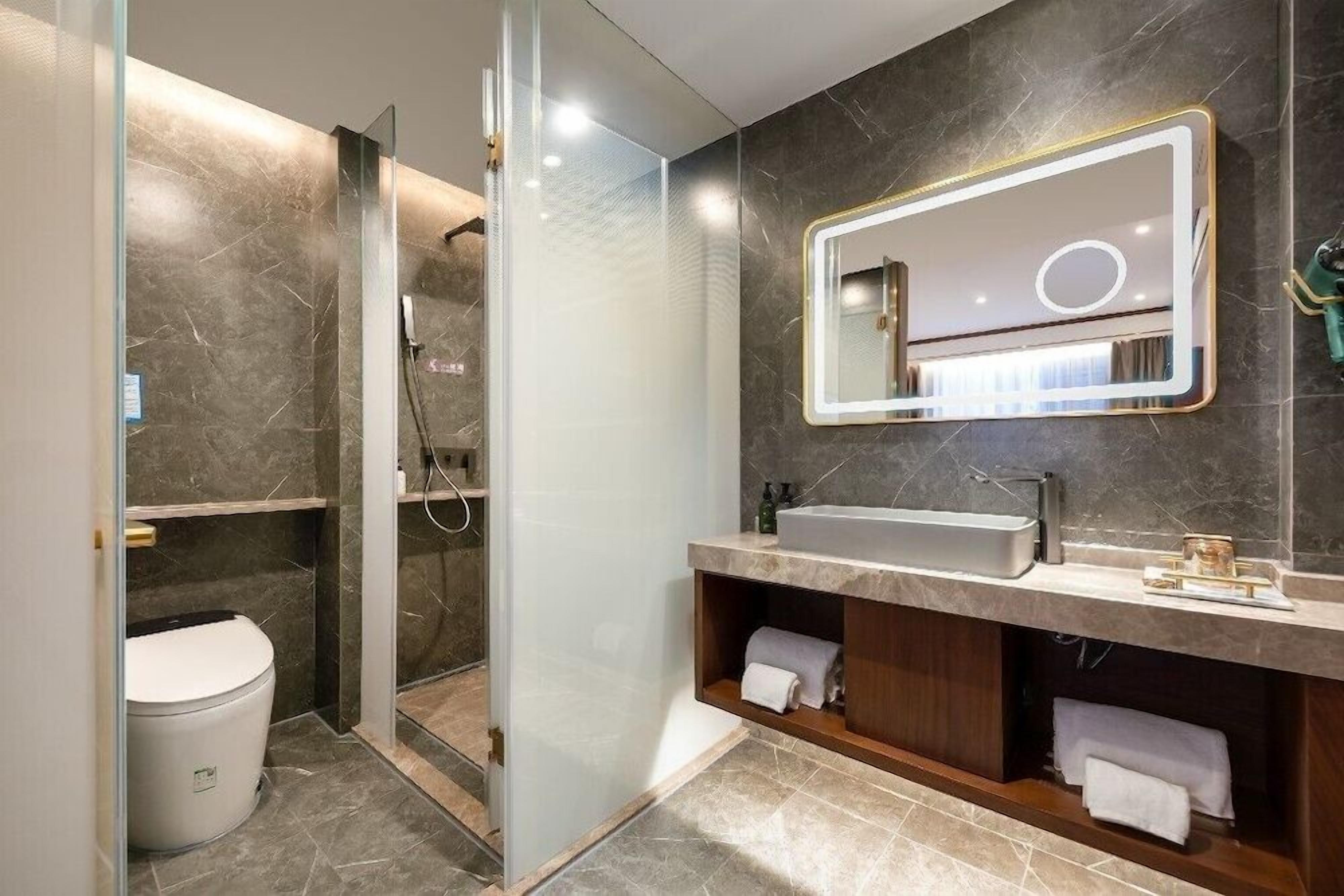 A modern bathroom with a glass-enclosed shower, a vanity with a sink, and a mirror with integrated lighting.