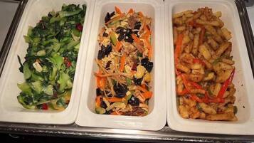 A buffet with three trays of food: greens, a mixed dish, and fried items.