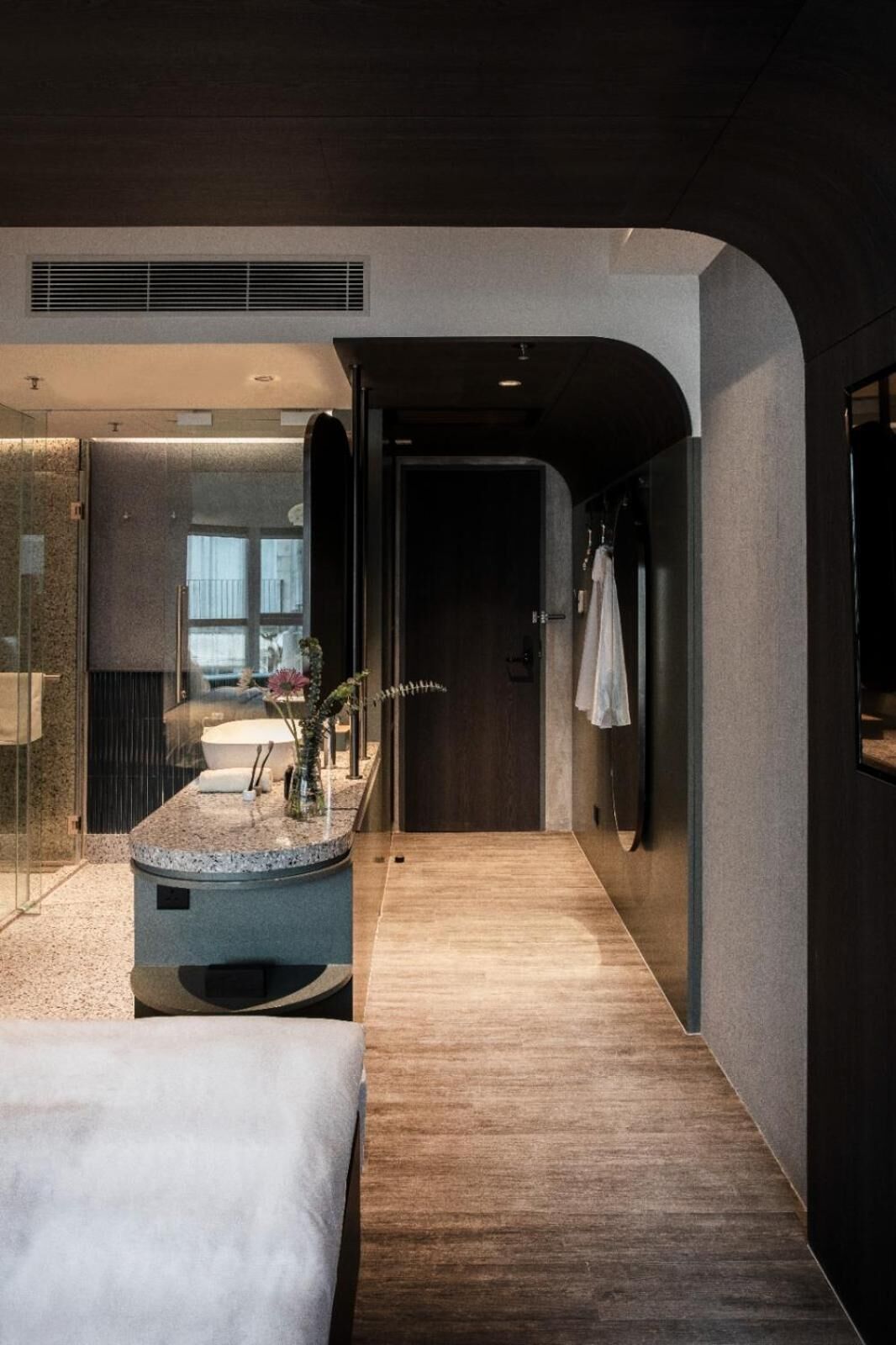 Une chambre d’hôtel moderne avec un plancher en bois, un grand lit, une salle de bain avec douche et un petit coin salon agrémenté d’une plante.