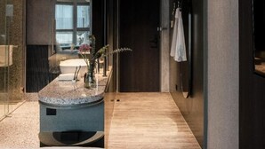 Habitació d'hotel moderna amb terra de fusta, un llit gran, un bany amb dutxa i una petita zona de seients amb una planta.