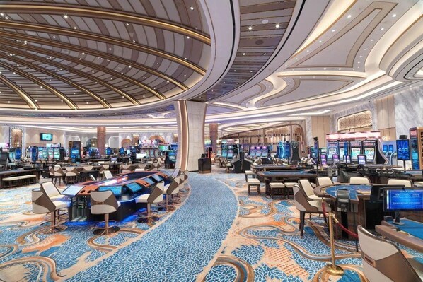 A casino with multiple gaming tables and slot machines, a central bar area, and a patterned carpet. - City of Dreams Mediterranean (Limassol)
