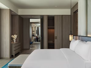 A modern hotel room with a large bed, a walk-in closet, and a view into the adjacent living area.